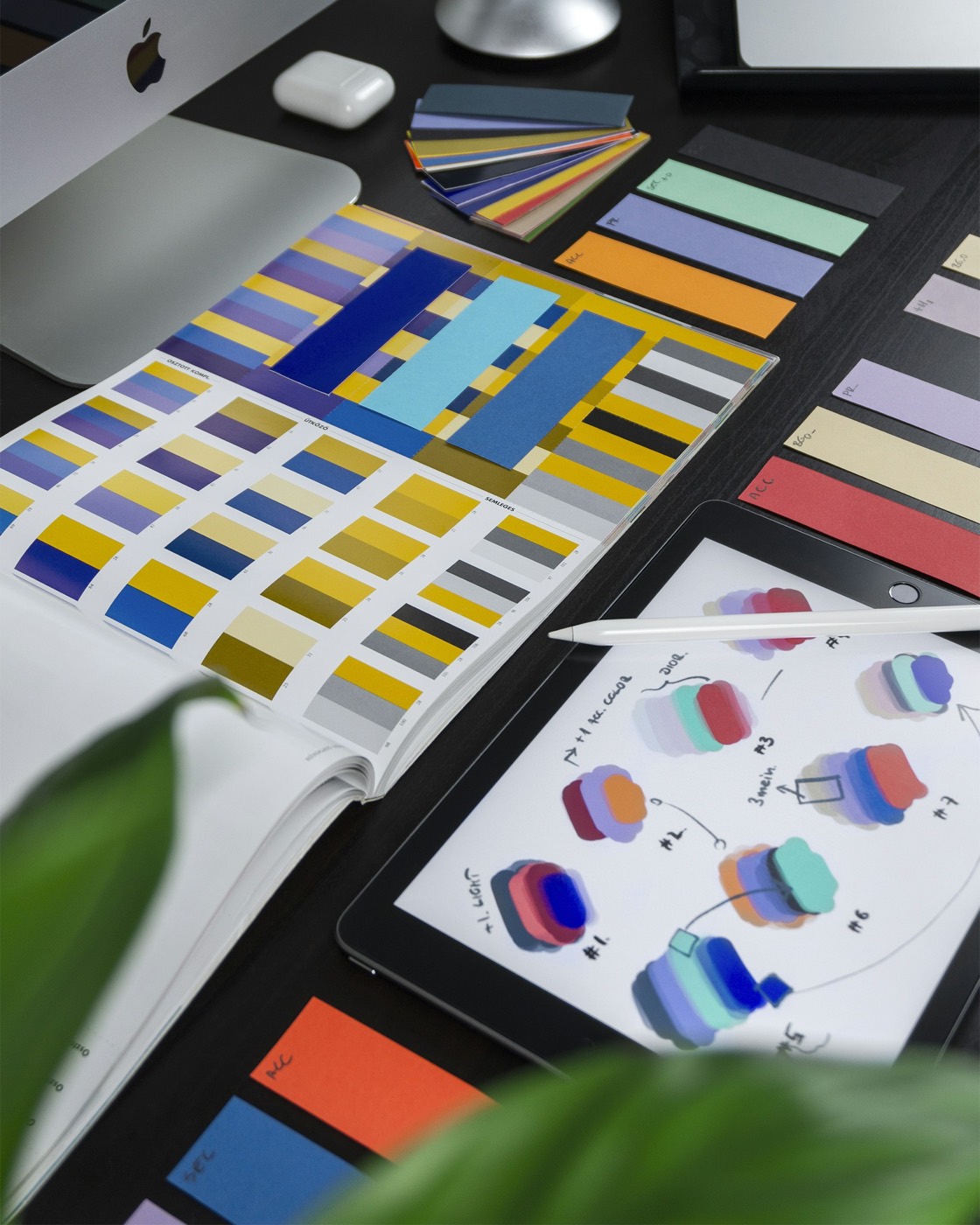 A designer's desk covered in color palette studies, swatch cards, and logo sketches on a tablet