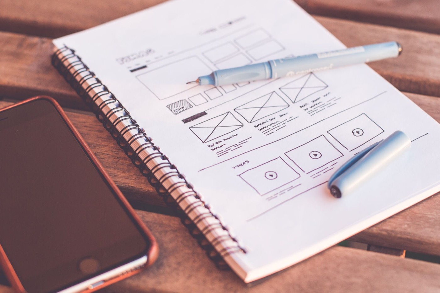 A notebook of pencil wireframe sketches for a website beside a phone